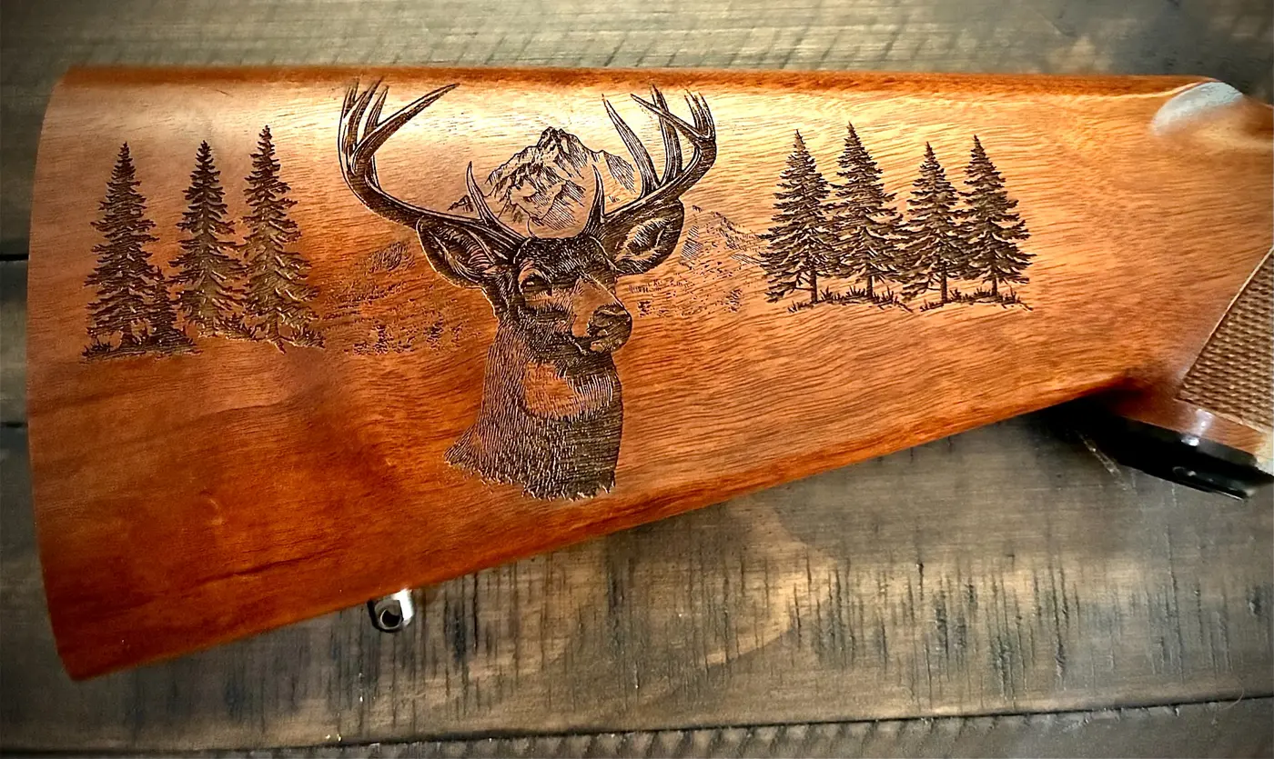 Wooden rifle stock engraved with a buck and trees